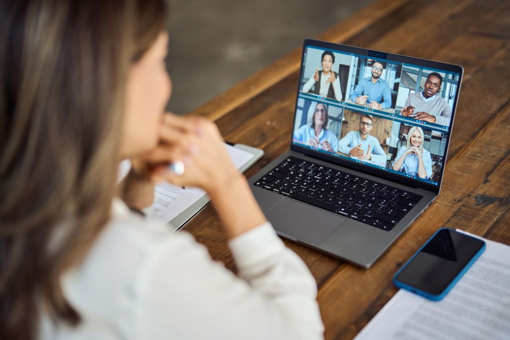 Business woman female team leader manager executive having remote workforce group meeting, remote workers discussing work plans by video digital conference call on laptop. Over shoulder view