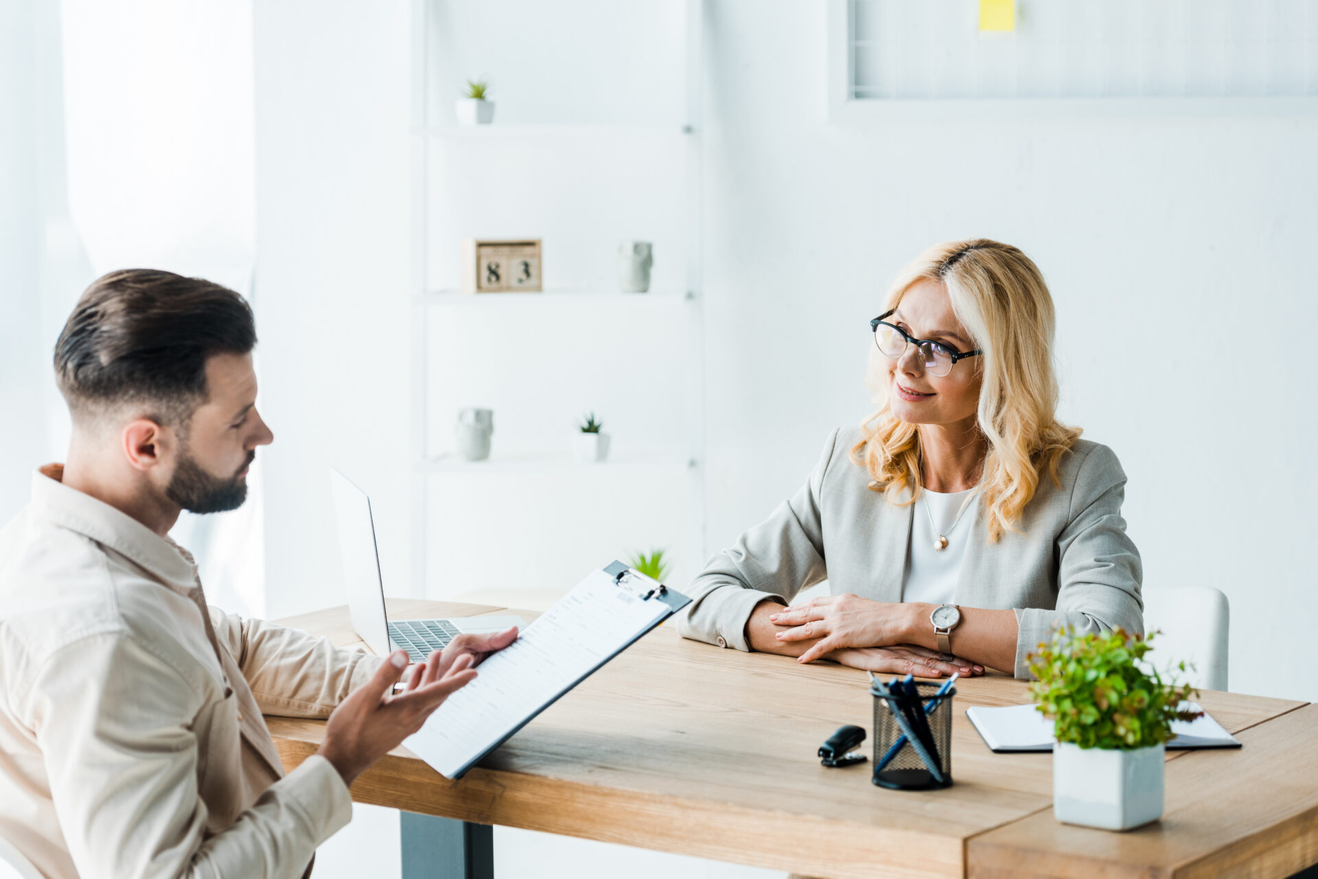 Woman recruiter folding her hands at a desk talking to a male candidate holding a clipboard