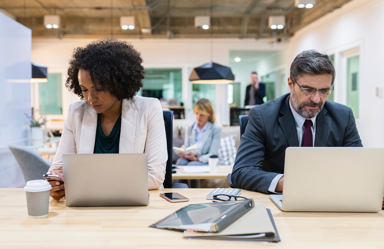 Two professionals looking at their laptops and cellphones