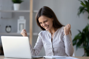 Smiling woman in front of her computer with her hands up