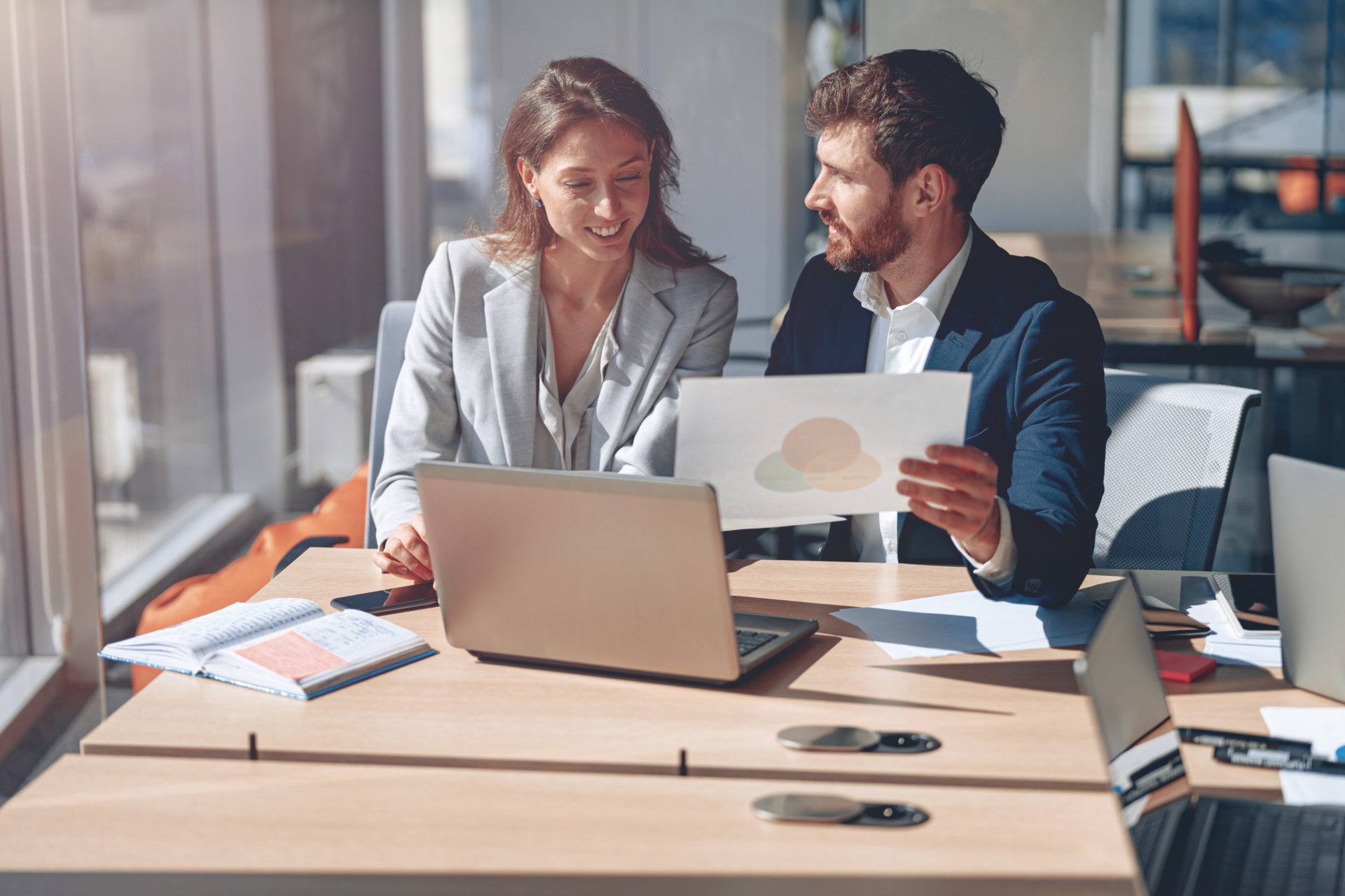 Female professional on laptop during a job audition sitting next to male manager showing her a venn diagram