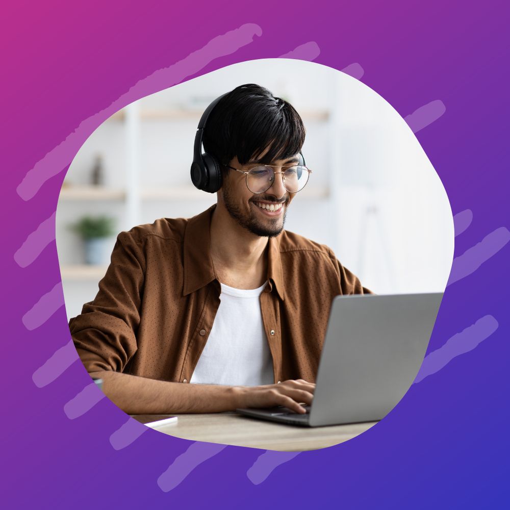 A young man wearing headphones and glasses, smiling while working on a laptop trying to find a non traditional career