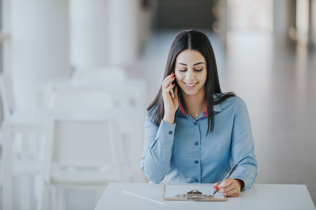 Recruiter calling a job candidate for a hard to fill position sitting at her white desk with a clipboard