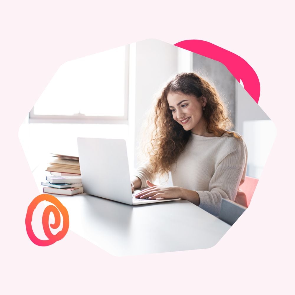 Female young professional sitting at a desk typing an email to a recruiter on a laptop next to a stack of books